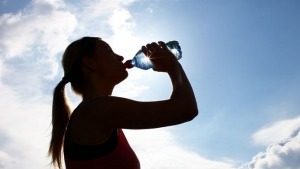 Gegenlichtaufnahme einer Frau, die aus einer Wasserflasche trinkt